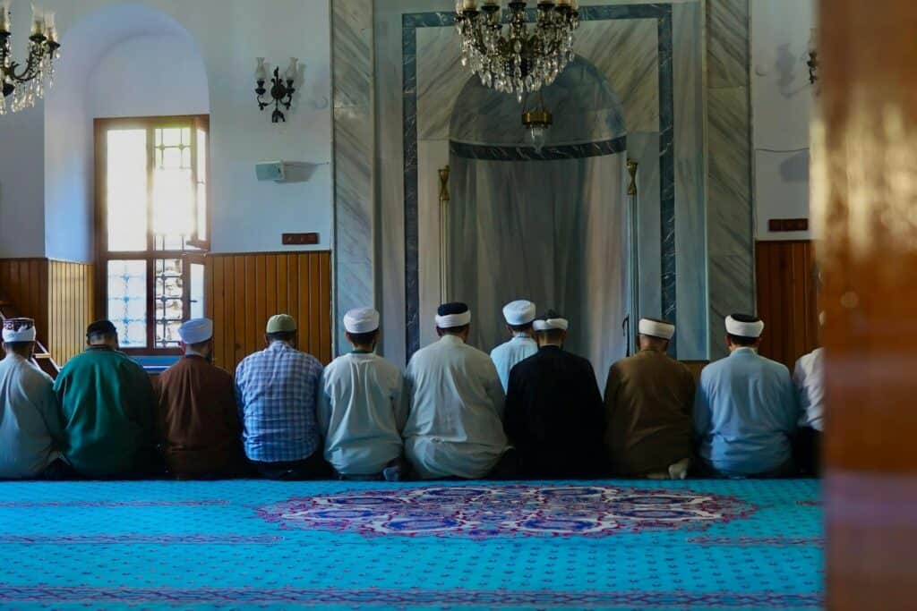 Prière musulmane collective à l'intérieur de l'Institut Anwar, salle de prière avec décoration marbrée et chandelier.